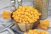 Poppin Popcorn Cheesy Cheddar popcorn in a bowl with ingredients all around it on a table.